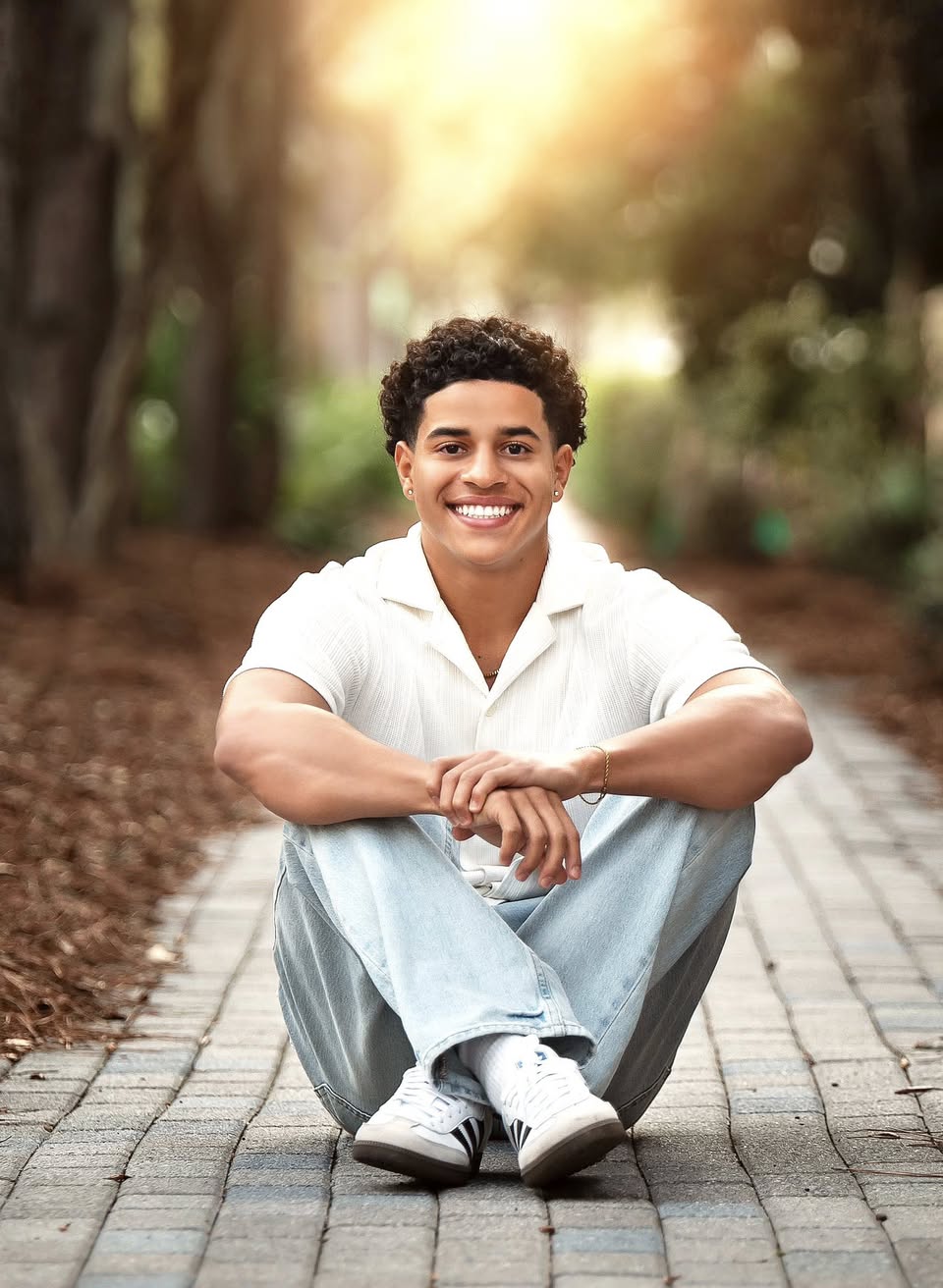 A high school senior sitting on a sunlit brick path at golden hour